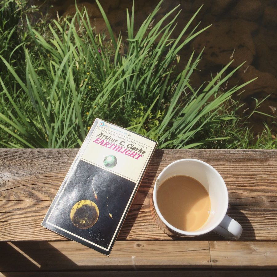 A vintage Arthur C. Clarke science fiction paperback and a mug of coffee on a sunny wooden railing