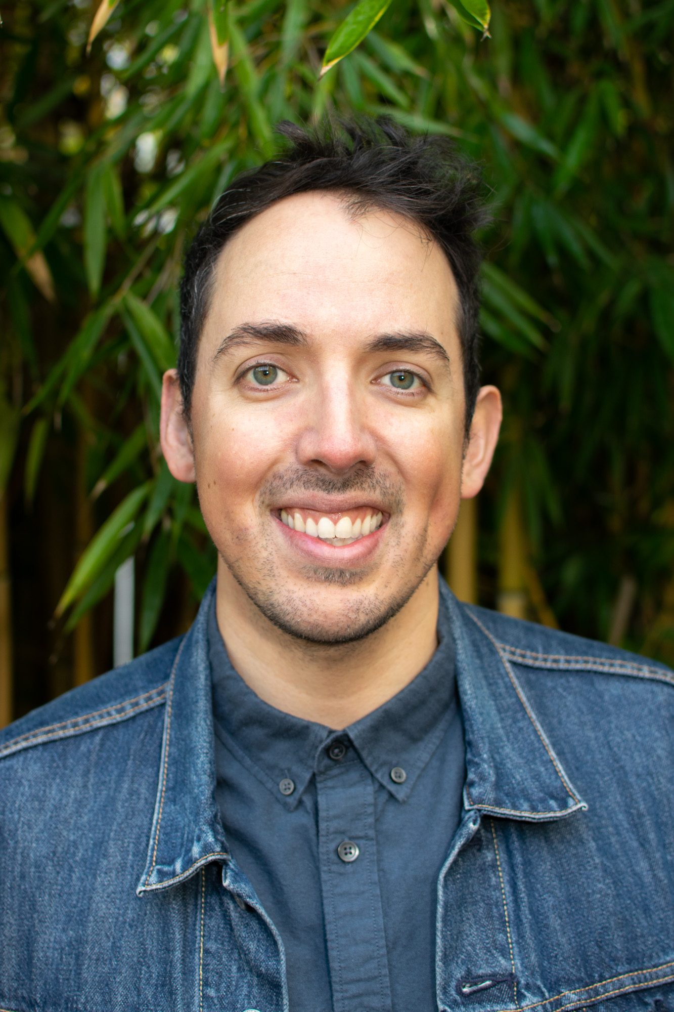 James Davidson smiling in a denim jacket in front of green bamboo